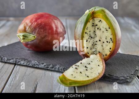 Frutta di cactus di mela peruviana intera e tagliata su supporto di legno su tavola grigia. Nome scientifico Cereus repandus Foto Stock