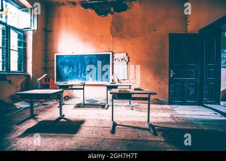 Classe abbandonata con scrivanie di fronte a una lavagna d'epoca Foto Stock