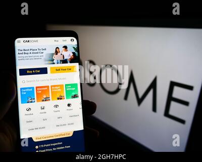 Persona che tiene smartphone con sito web della società malese piattaforma auto usate Carsome Group sullo schermo con logo. Concentrarsi sul centro del display del telefono.