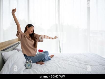 La giovane donna si rilassa e si stende le braccia sul letto a casa. Fitness mattutino, concetto di consapevolezza. Foto Stock