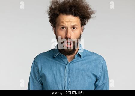 ritratto di giovane uomo scioccato in denim camicia apertura bocca e fare un volto stupito mentre si posa su sfondo grigio in studio Foto Stock