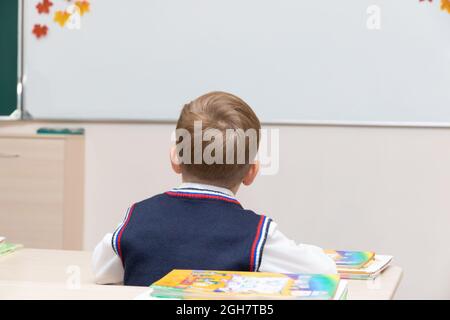 Un ragazzo primo-grader alla sua scrivania in classe il giorno di conoscenza il 1 settembre a scuola in lezione sullo sfondo di una lavagna bianca Foto Stock