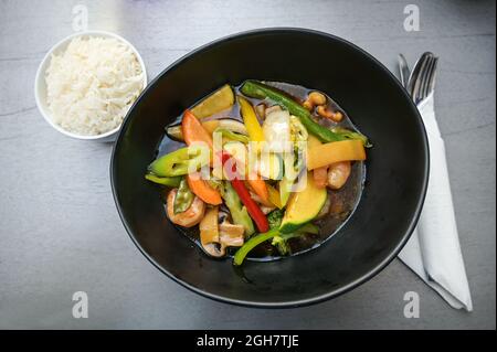 Verdure e gamberi in salsa teriyaki in una ciotola nera servita con riso su un tavolo grigio, alto angelo vista dall'alto, fuoco selezionato Foto Stock