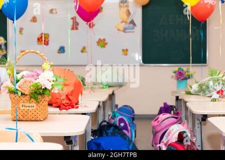 Lezione di scuola il 1 settembre senza studenti con palloncini colorati e fiori su scrivanie sullo sfondo del consiglio di scuola. Le iscrizioni Foto Stock