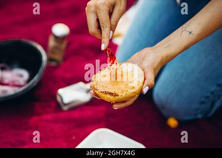 Primo piano immagine della ragazza mano mettere salsa su Burger Bun. Barbecue all'aperto Foto Stock