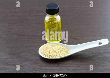 Bottiglia di olio di sesamo e semi di sesamo in un cucchiaio di ceramica bianca su sfondo di legno nero Foto Stock