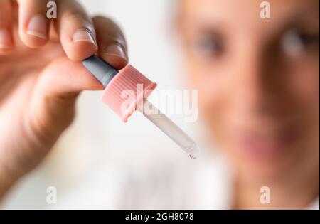 Donna che tiene una pipetta contagocce sublinguale olio di cannabis e la fa cadere in bocca. Donna malata o malata giovane usando una goccia per la medicina Foto Stock