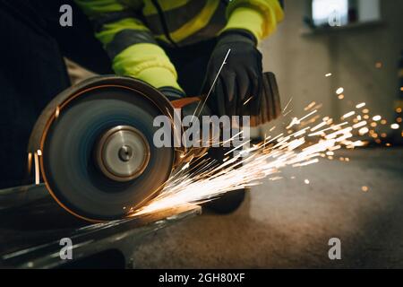 Lavoratrice femminile che utilizza la sega elettrica durante il taglio del metallo in cantiere Foto Stock