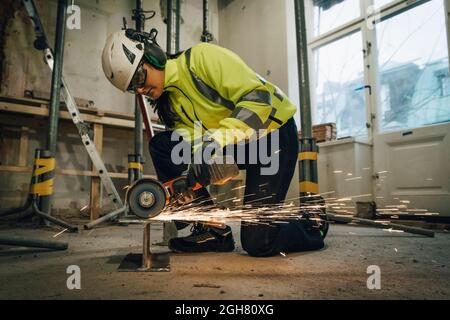 Intera lunghezza di lavoratrice di costruzione femminile che taglia il metallo mentre usa la sega elettrica nel luogo Foto Stock