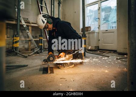 Intera lunghezza del lavoratore di costruzione maschio usando la sega elettrica mentre taglia il metallo sul luogo Foto Stock