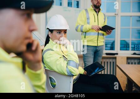 Una donna pensierosa che lavora con un tablet digitale in ufficio durante la riunione Foto Stock