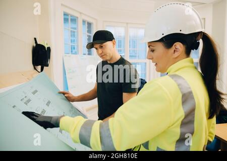 Appaltatore di costruzione femminile che discute sopra il blueprint con il lavoratore maschio in ufficio Foto Stock