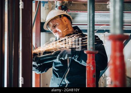 Lavoratrice di costruzione maschile che taglia il metallo con macchinari in loco Foto Stock