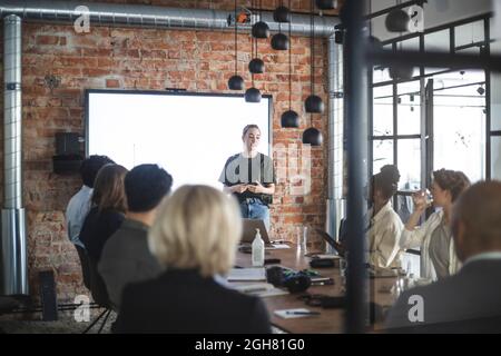 Giovane donna d'affari che presenta i colleghi durante l'incontro in ufficio Foto Stock