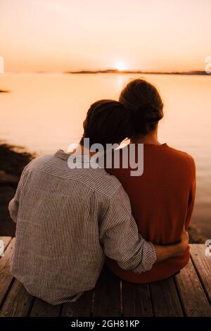 Vista posteriore di amici maschi che guardano il tramonto mentre si siedono sul molo Foto Stock