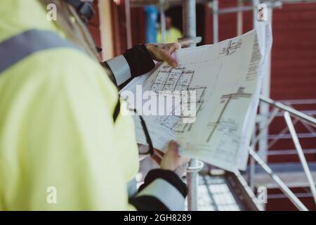 Imprenditore di costruzione femminile che legge piano di pavimento in cantiere Foto Stock