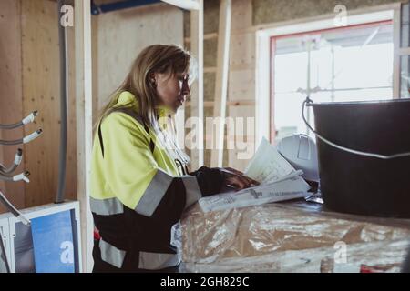 Bionda imprenditore di costruzione femminile che analizza la pianta del pavimento in cantiere Foto Stock