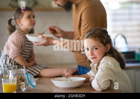 Padre con le figlie in casa, mangiare la colazione in cucina. Foto Stock
