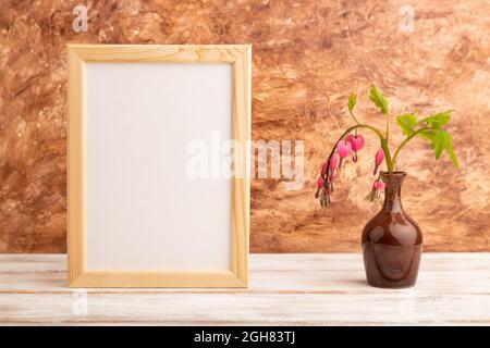 Telaio in legno con dicentra rosa, cuore rotto in vaso di ceramica su fondo di cemento marrone. Vista laterale, copia spazio, mockup, dima, molla, estate mi Foto Stock