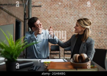 Cheerful Down sindrome uomo con donna d'affari collega che lavora in ufficio, inclusione sociale e concetto di cooperazione. Foto Stock