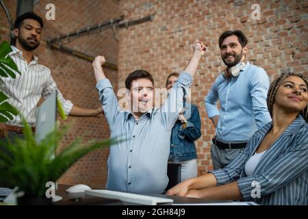 Happy Down sindrome uomo con uomini d'affari in ufficio, inclusione sociale e concetto di cooperazione. Foto Stock