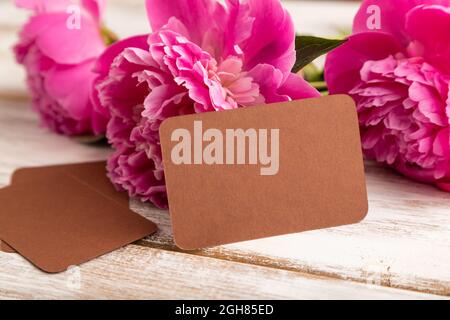 Biglietto da visita marrone con fiori rosa di peonia su sfondo bianco in legno. Vista laterale, spazio copia, vita morta. Colazione, mattina, concetto di primavera. Foto Stock