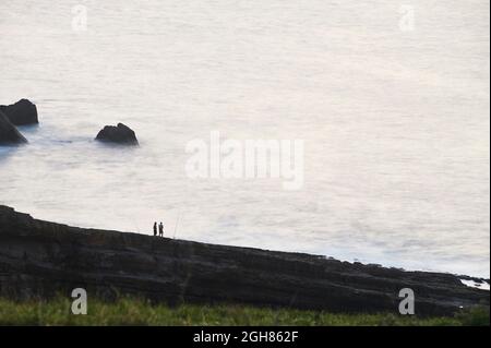 Pescatori sulle rocce della costa cantabrica al tramonto Foto Stock