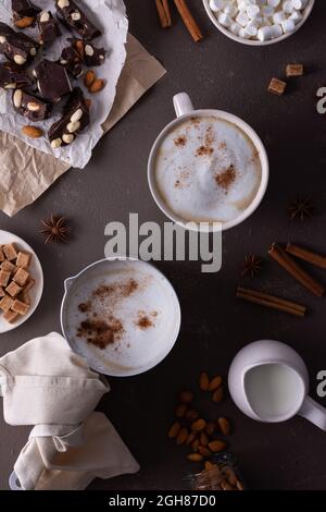 Bevanda di cacao invernale con schiuma di latte e marshmallow in una tazza e un cucchiaio di alluminio, cannella e mandorle, cioccolato fondente con noci Foto Stock