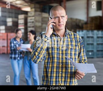 Uomo che parla al telefono e che tiene il documento in mano. Due donne si sono levate in piedi e discutono. Foto Stock