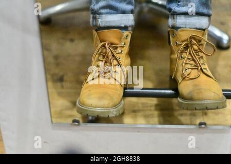 Una vista speculare di un paio di piedi in stivali cammello indossati poggiati su un poggiapiedi con jeans ribaltati, con lacci lunghi in archi Foto Stock