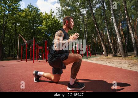 Atletico uomo barbuto fare affondi su terreno sportivo Foto Stock