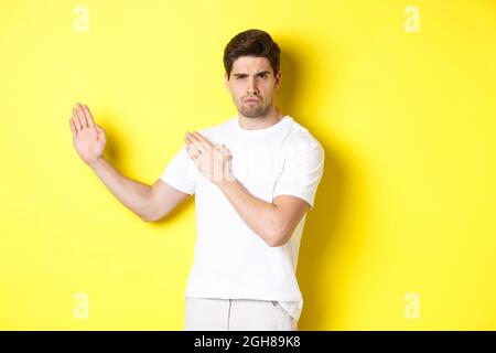 Uomo che mostra abilità kung-fu, arti marziali movimento ninja, in piedi in bianco t-shirt pronto a combattere, in piedi su sfondo giallo Foto Stock