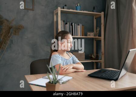 Studentessa adolescente che fa i compiti con il portatile a casa. Il bambino usa i gadget per lo studio, si siede al tavolo guardando una lezione video o una trasmissione dal vivo Foto Stock