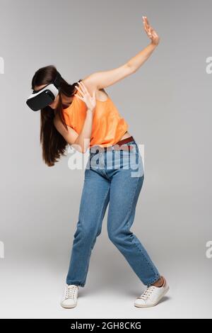 tutta la durata della giovane donna spaventato in visore vr che gesta in grigio Foto Stock
