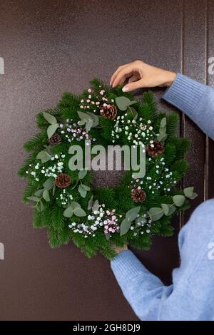 Hipster persona che decora la porta anteriore con la corona di Natale Foto Stock