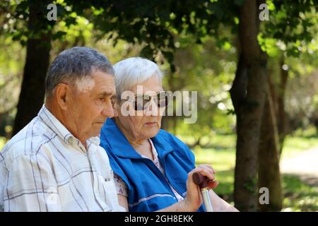 Coppia anziana seduta con bastoni da passeggio su una panca. Tempo libero nel parco, vita in pensione Foto Stock