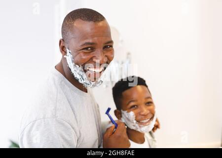 Ritratto di sorridente padre afroamericano con figlio divertirsi con la schiuma da barba in bagno Foto Stock