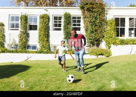 Padre afroamericano con figlio divertirsi e giocare a calcio in giardino Foto Stock