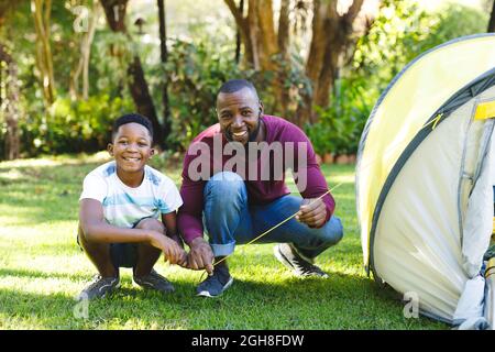 Ritratto di padre afro-americano con figlio che ha divertimento e pitching tenda in giardino Foto Stock