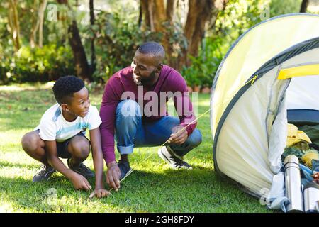 Padre africano americano con figlio che ha divertente pitching tenda in giardino Foto Stock