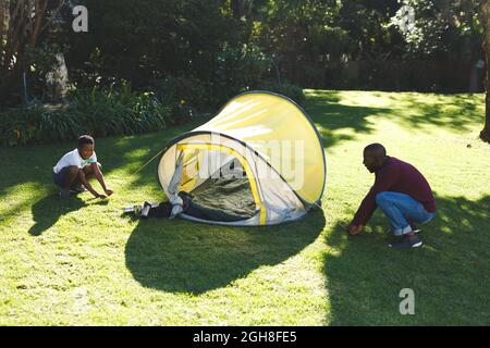 Papà afroamericano con figlio che ha divertimento e pitching tenda in giardino soleggiato Foto Stock