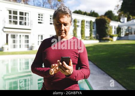 Felice uomo caucasico anziano utilizzando smartphone in giardino soleggiato Foto Stock