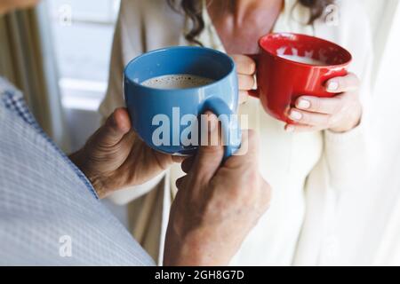 Coppia caucasica anziana in piedi accanto alla finestra, tenendo le tazze Foto Stock