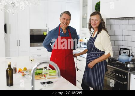 Ritratto di sorridente coppia caucasica senior indossando grembiuli in cucina moderna Foto Stock