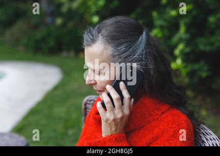 Felice anziana donna caucasica che parla su smartphone in giardino Foto Stock