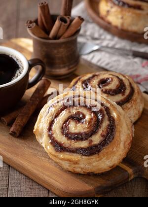 Dolci alla cannella glassati con tazza di caffè e bastoncini di cannella su un tagliere di legno Foto Stock