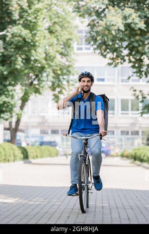 Corriere musulmano positivo che parla su smartphone mentre si guida bile su strada urbana Foto Stock