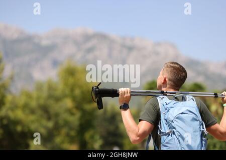 Il giovane uomo si trova in cima alla montagna e tiene i bastoni da nordic walking Foto Stock