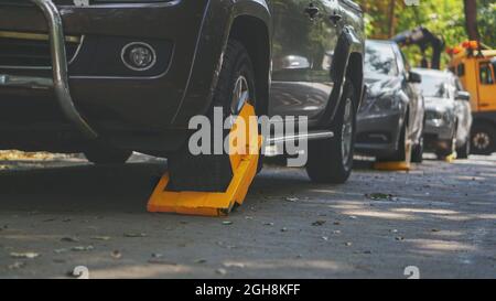 Un'auto parcheggiata con un blocco pneumatico giallo per la violazione di parcheggio illegale. Bloccaggio delle ruote in un'area limitata per il parcheggio. Foto Stock