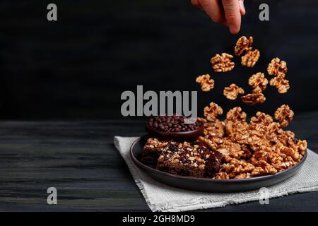 Le noci cadono in un piatto con pezzi di brownie di cioccolato e noci Foto Stock